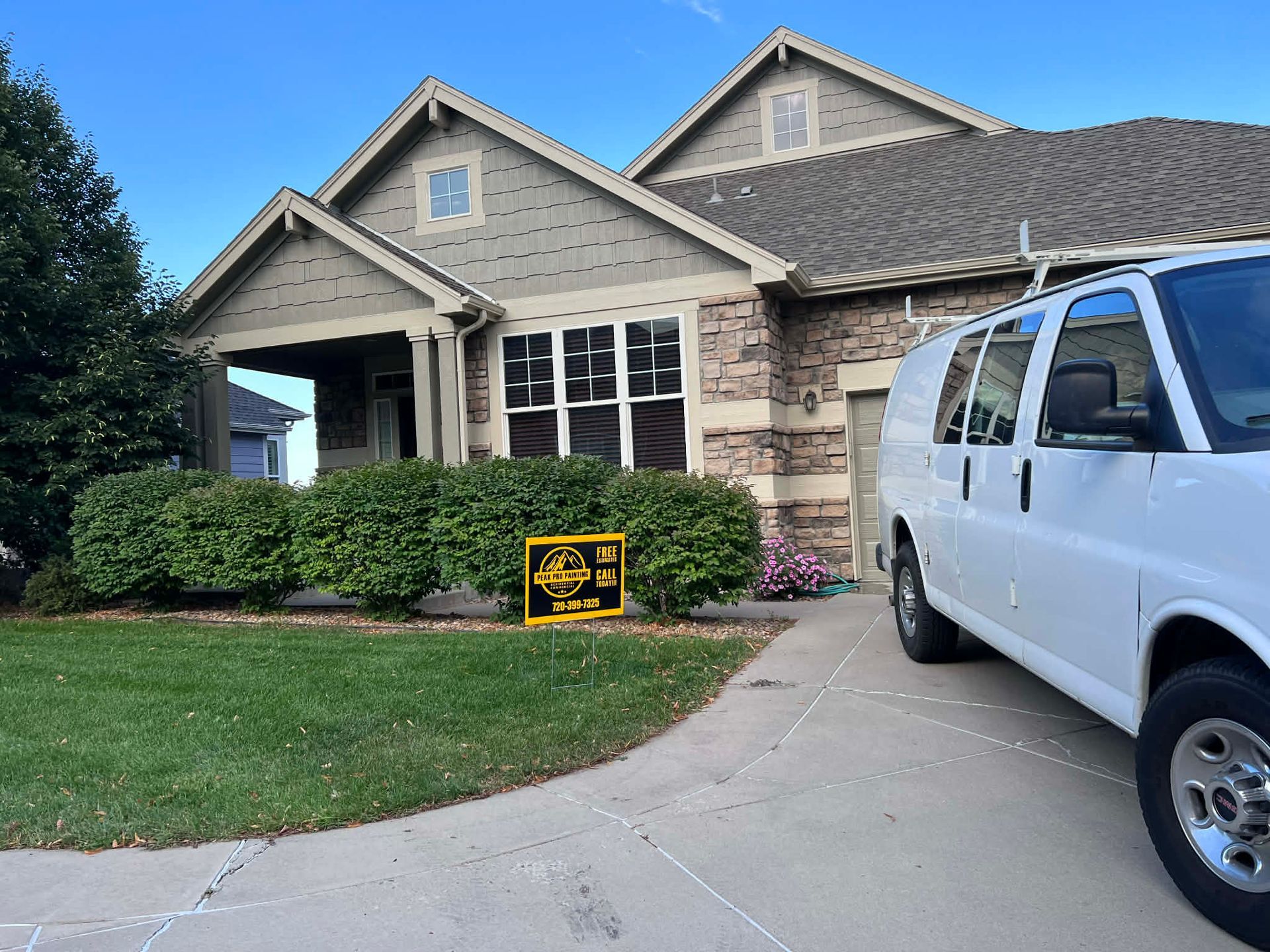 A beige suburban house with a white work van parked in the driveway and a yellow sign in front of the bushes.