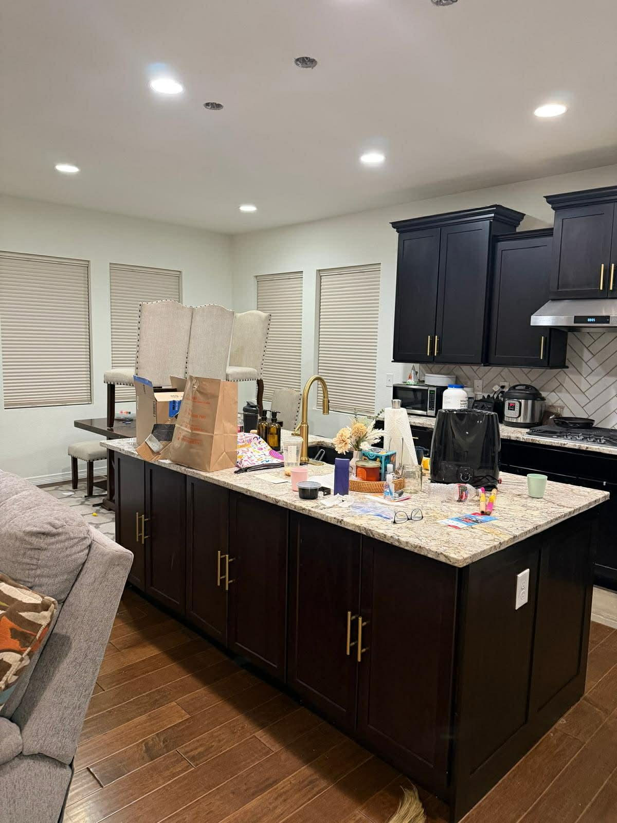 A kitchen island with dark cabinets and a granite countertop, cluttered with various items, next to a dining area.