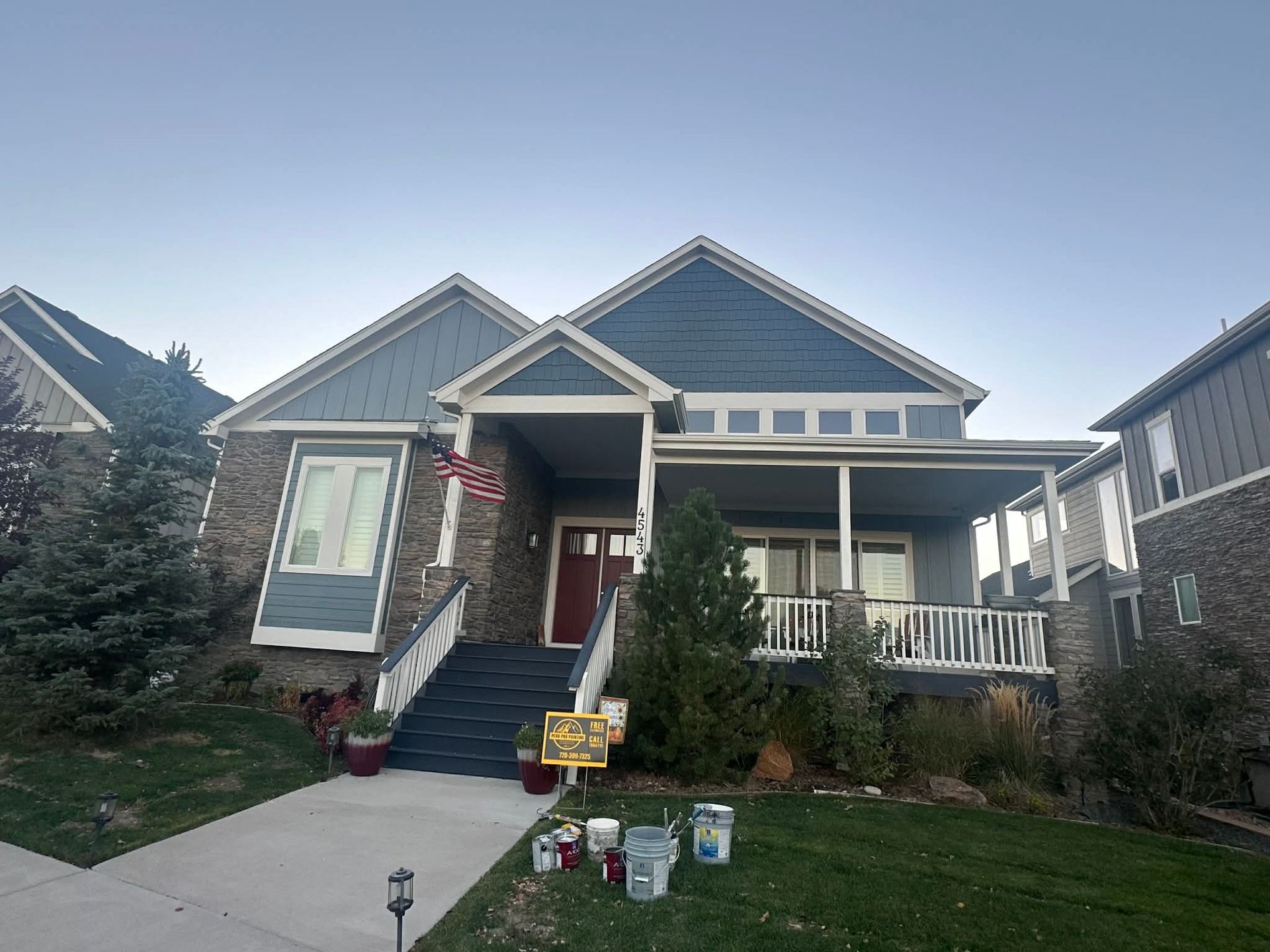 A blue, multi-gabled suburban home with stone accents, a red front door, a porch, and stairs leading to the entrance.