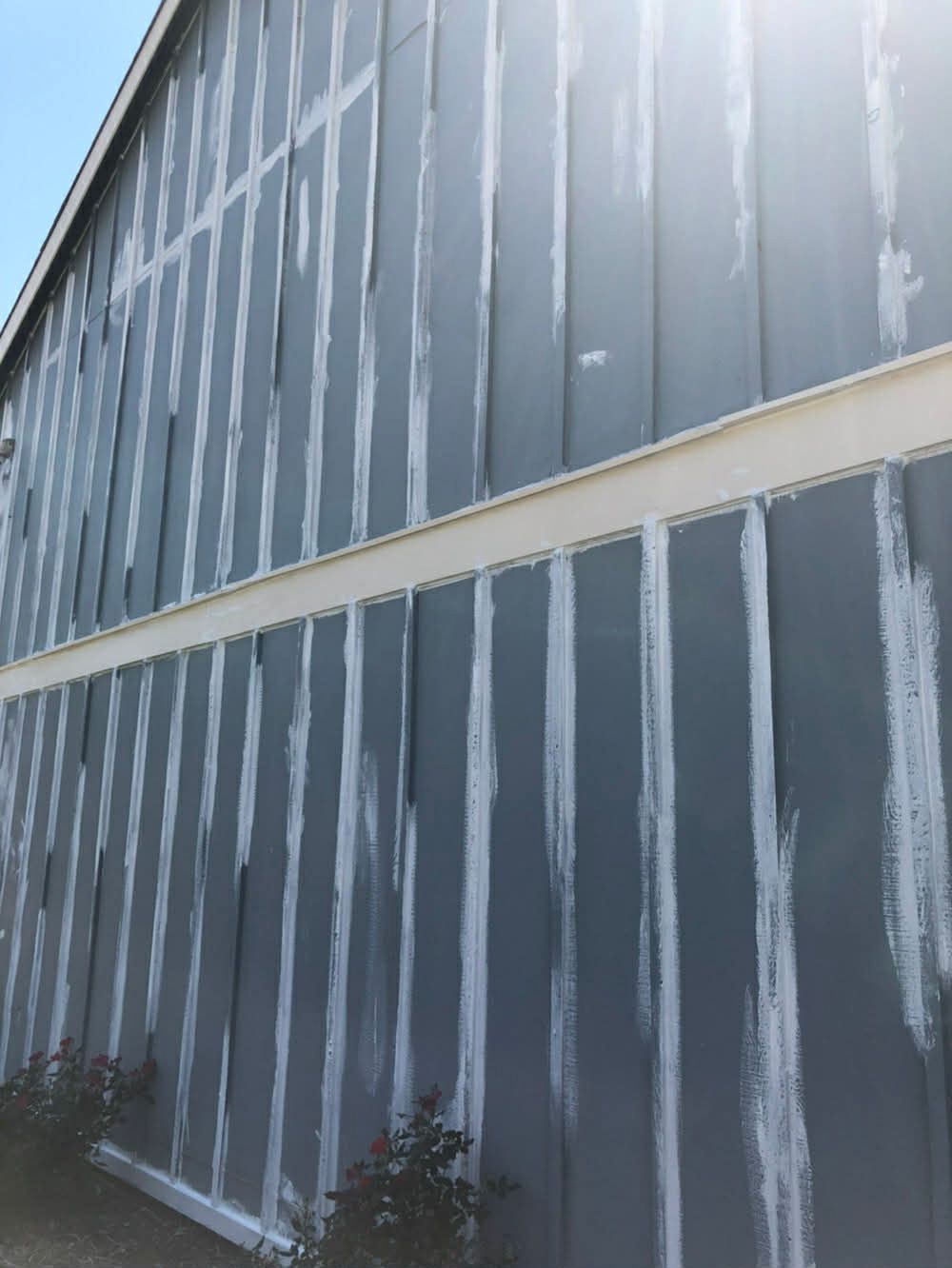 A multi-story exterior wall with grey vertical siding panels, featuring prominent white sealant at the joints.
