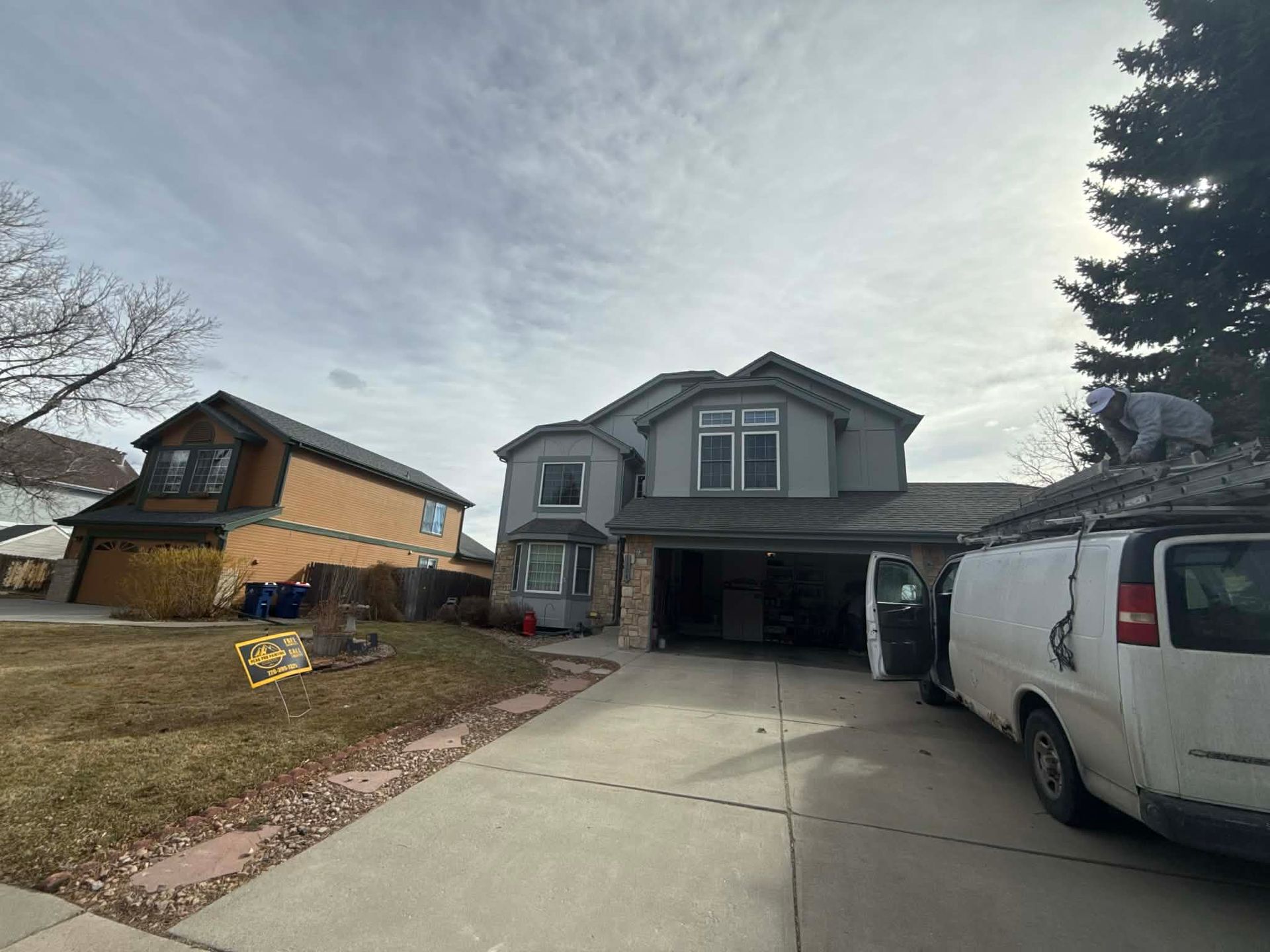 A white service van parked in a residential driveway, with a worker on the roof of the vehicle next to a two-story home.