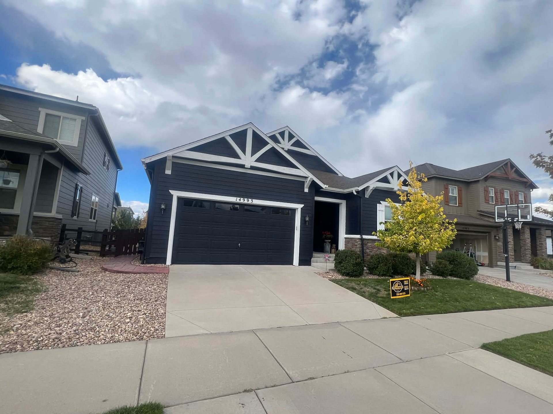 A dark blue single-story home with white trim and a prominent gabled roof, set between two other suburban houses.