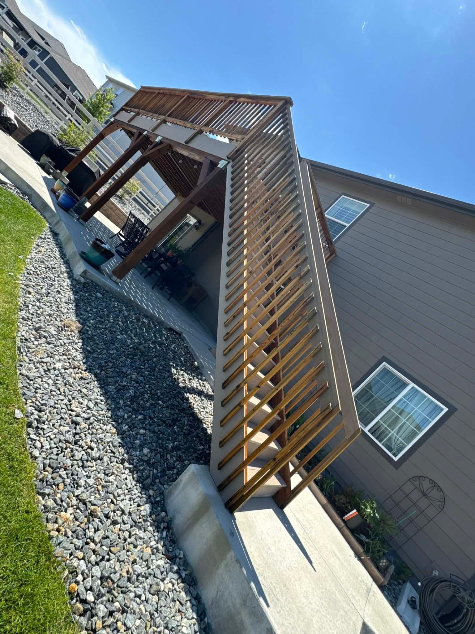 A backyard view of a wooden deck with a staircase leading down to a concrete patio next to a two-story brown house.