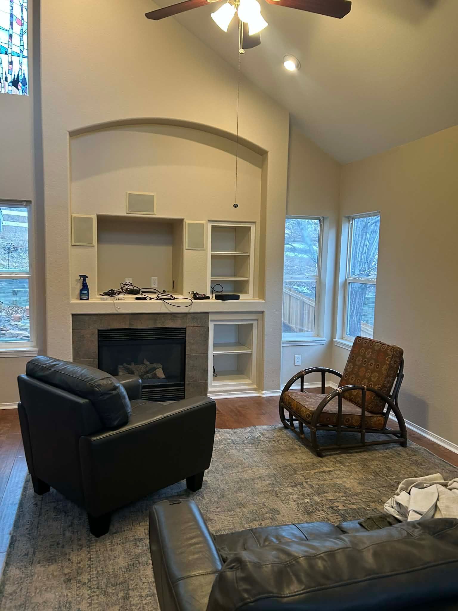 Living room with a fireplace, built-in shelving, two chairs, and a patterned rug under a vaulted ceiling with a fan.