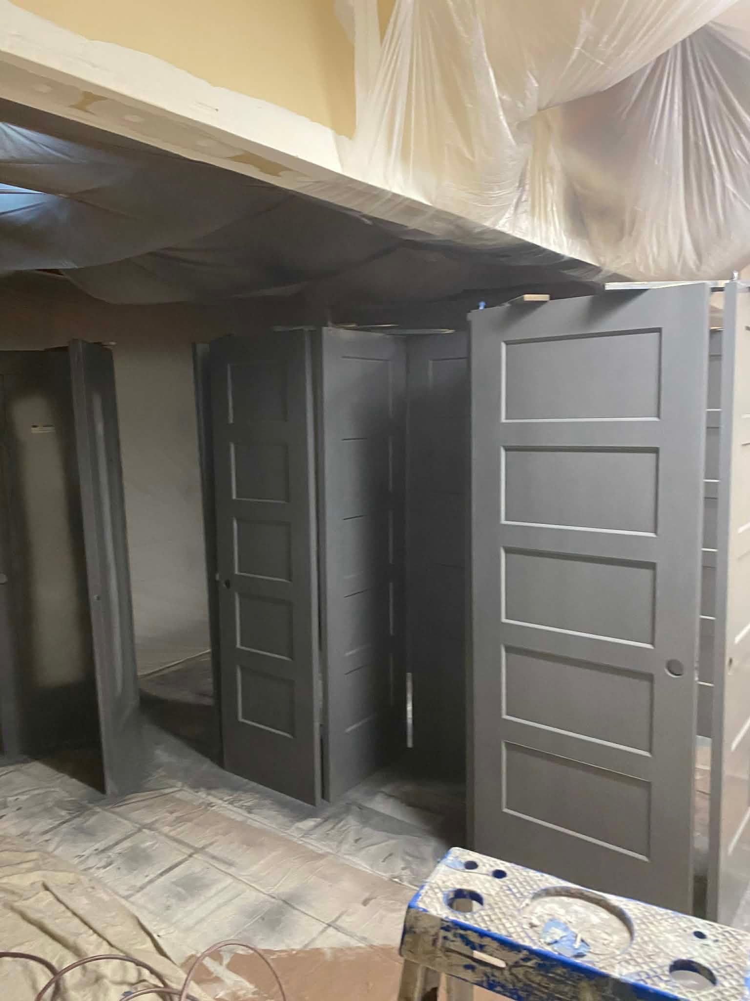 Several newly painted gray, five-panel doors stand in a room draped with plastic sheets for a home improvement project.