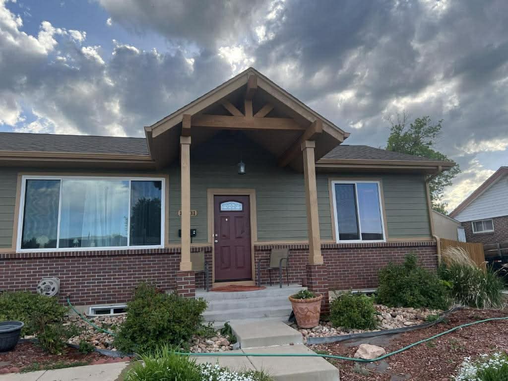 A one-story home with dark brown siding and brick, a wood-trimmed front entrance, and large windows under a cloudy sky.