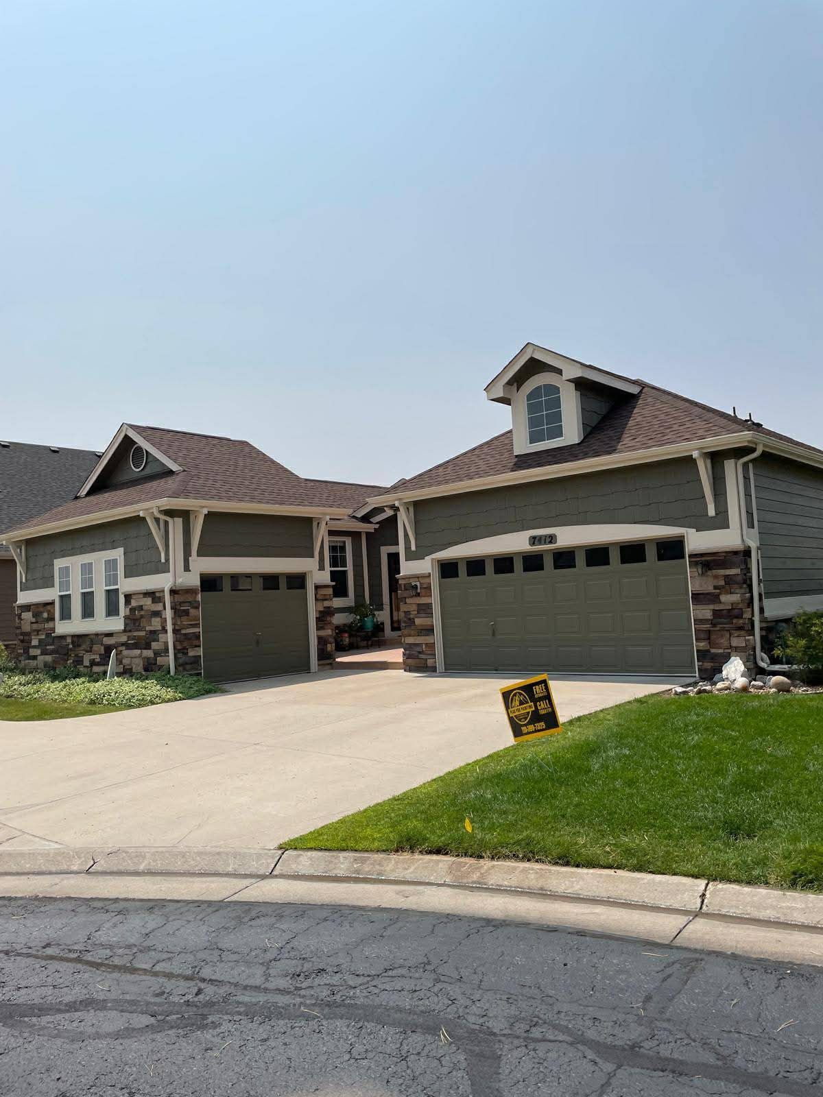 A dark green, single-story house with a two-car garage, stone trim, and gabled roofline from the street view.