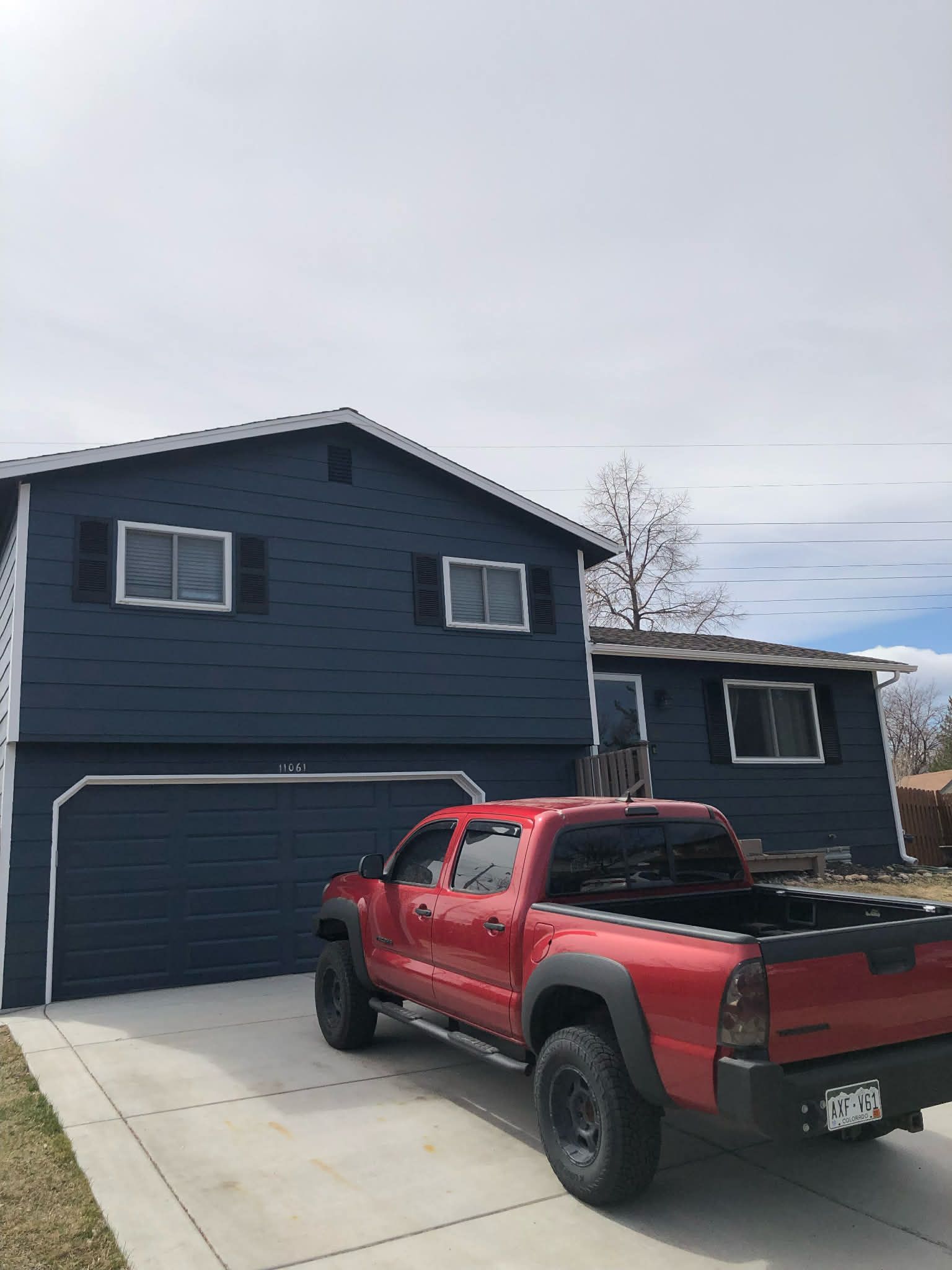 A red pickup truck is parked in the driveway of a two-story house with dark blue horizontal siding.