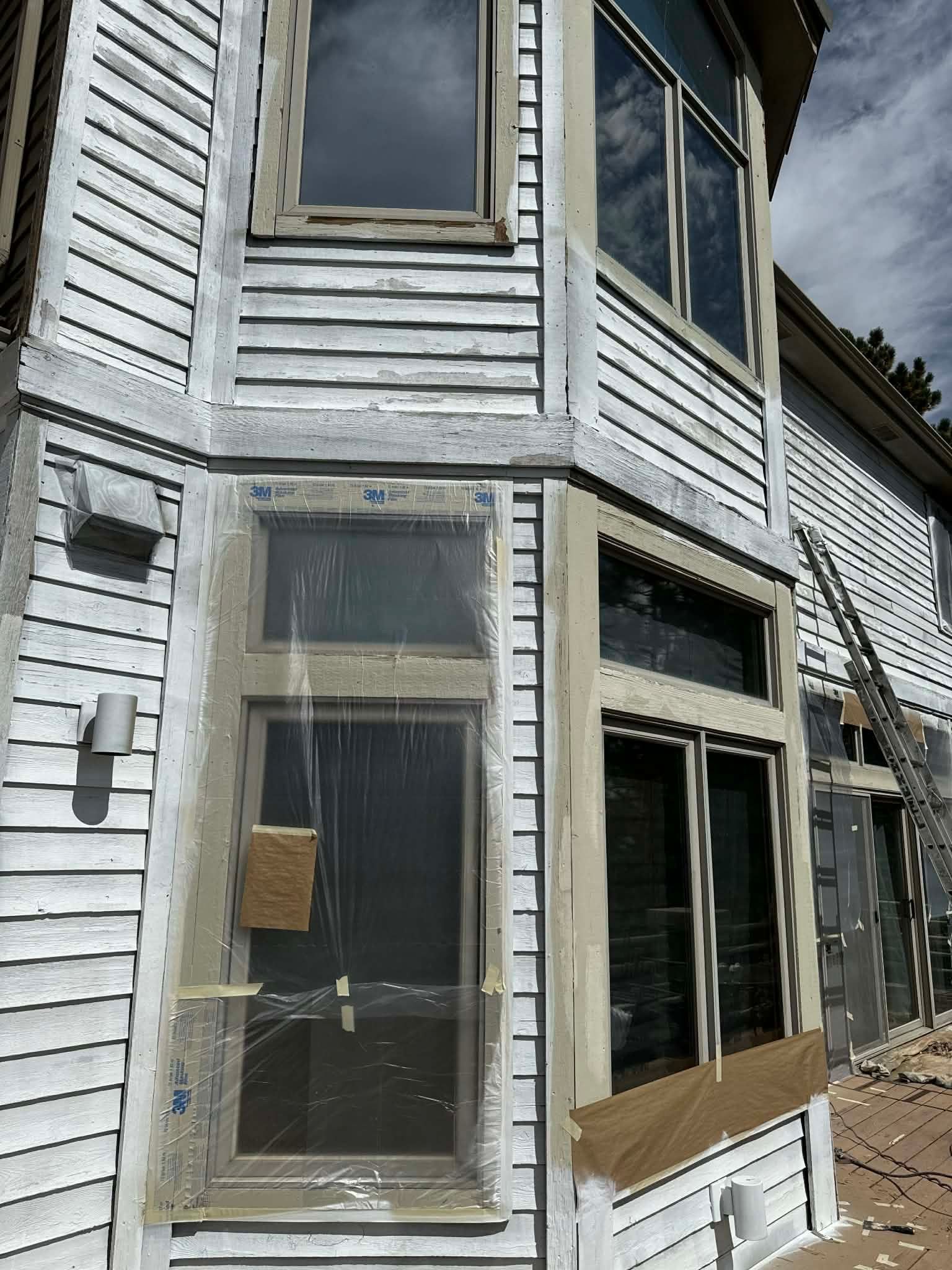 A multi-story house under renovation with white siding, unfinished wooden trim, and plastic-covered windows.