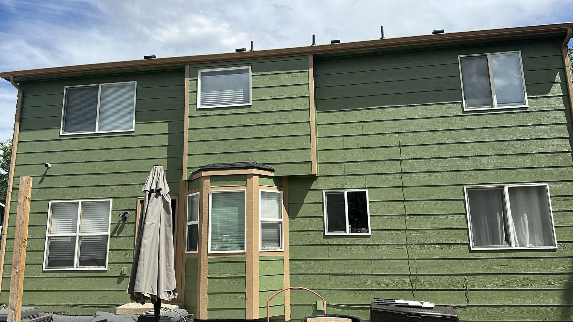 A two-story house exterior under construction, covered in green wall sheathing with installed windows and framing.