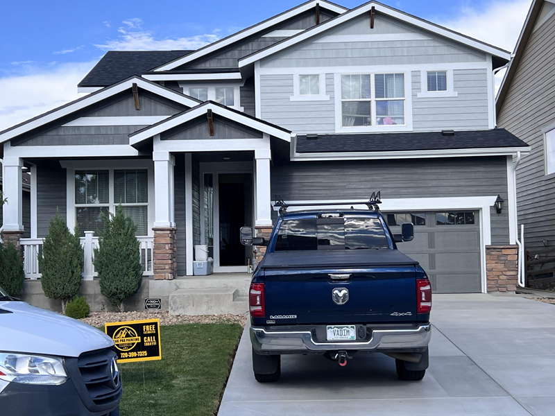 A two-story gray house with a front porch, a garage, and a blue pickup truck parked in the driveway.