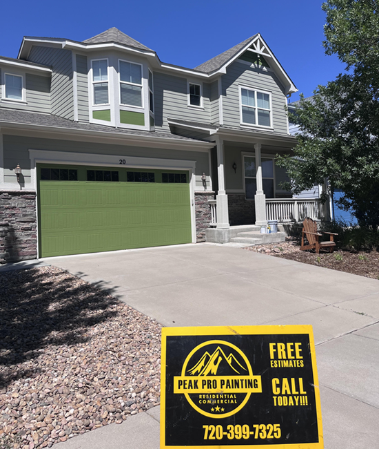 A residential house with a green garage door and siding, with a Peak Pro Painting sign in the foreground.