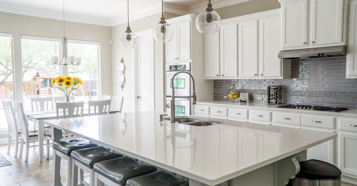 Bright, modern kitchen with white cabinets, a large white island with stools, and a sunlit dining area with sunflowers.