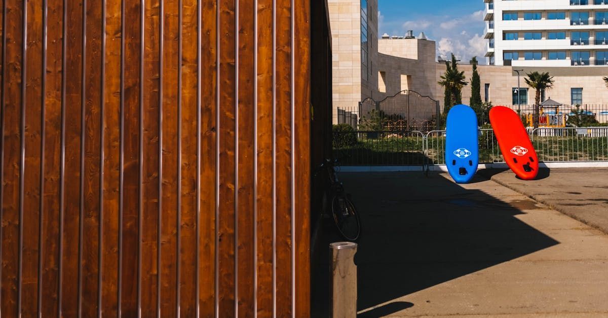 A blue and a red surfboard lean against a wooden wall near an outdoor resort area.