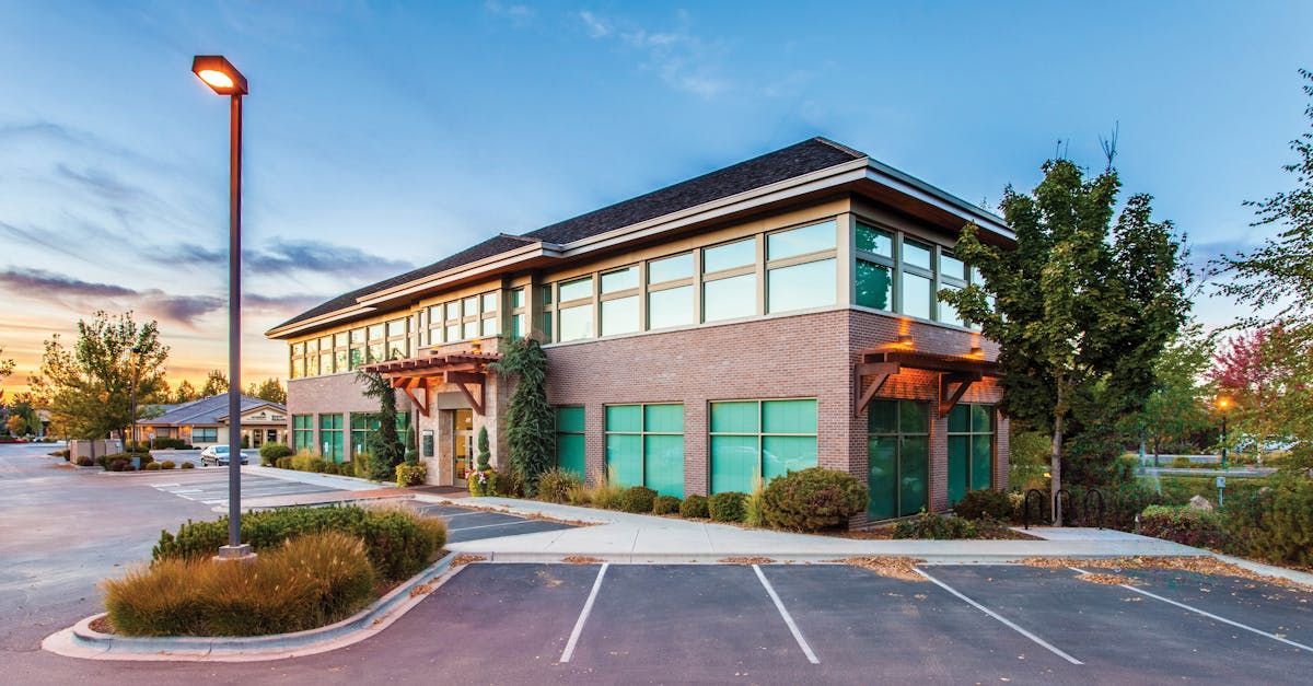A two-story brick office building with glass windows, framed by trees and a parking lot at twilight.