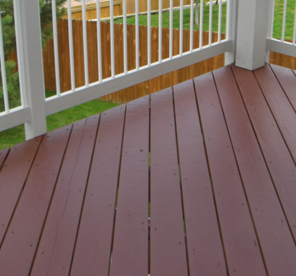 A brown wooden deck with white railing, viewed from a high angle looking out toward a backyard with a wooden fence.
