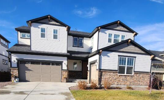 A two-story suburban house with white siding, stone veneer accents, dark trim, a two-car garage, and a concrete driveway.
