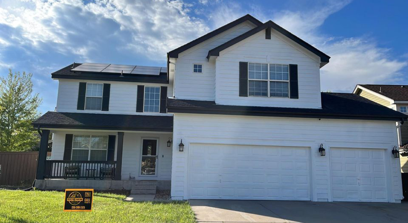 A white, two-story house with a three-car garage, black window shutters, and solar panels on a sunny day.