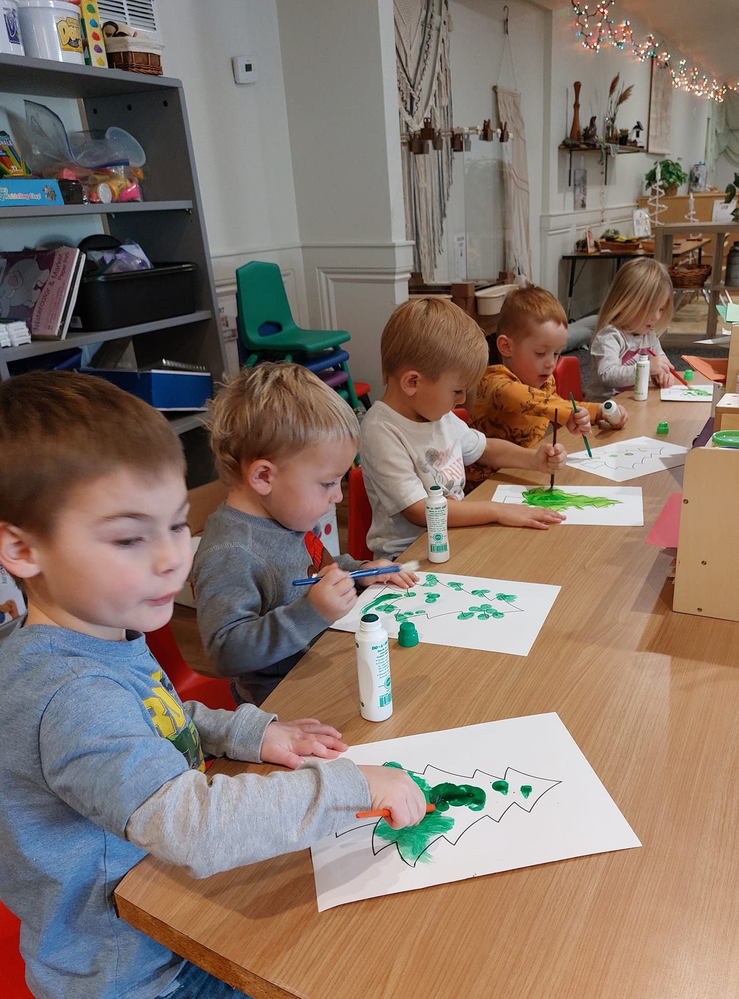 A group of young children are sitting at a table painting.