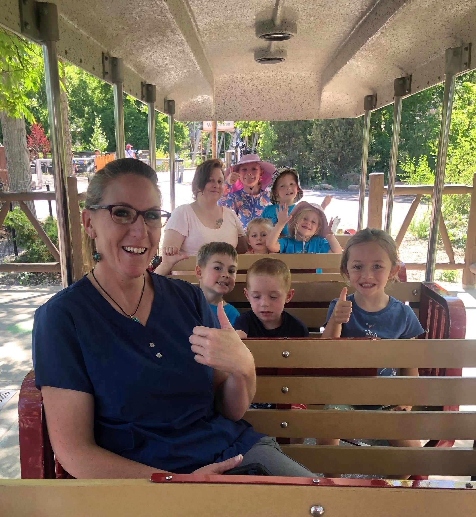 A woman is giving a thumbs up while sitting on a train with children.