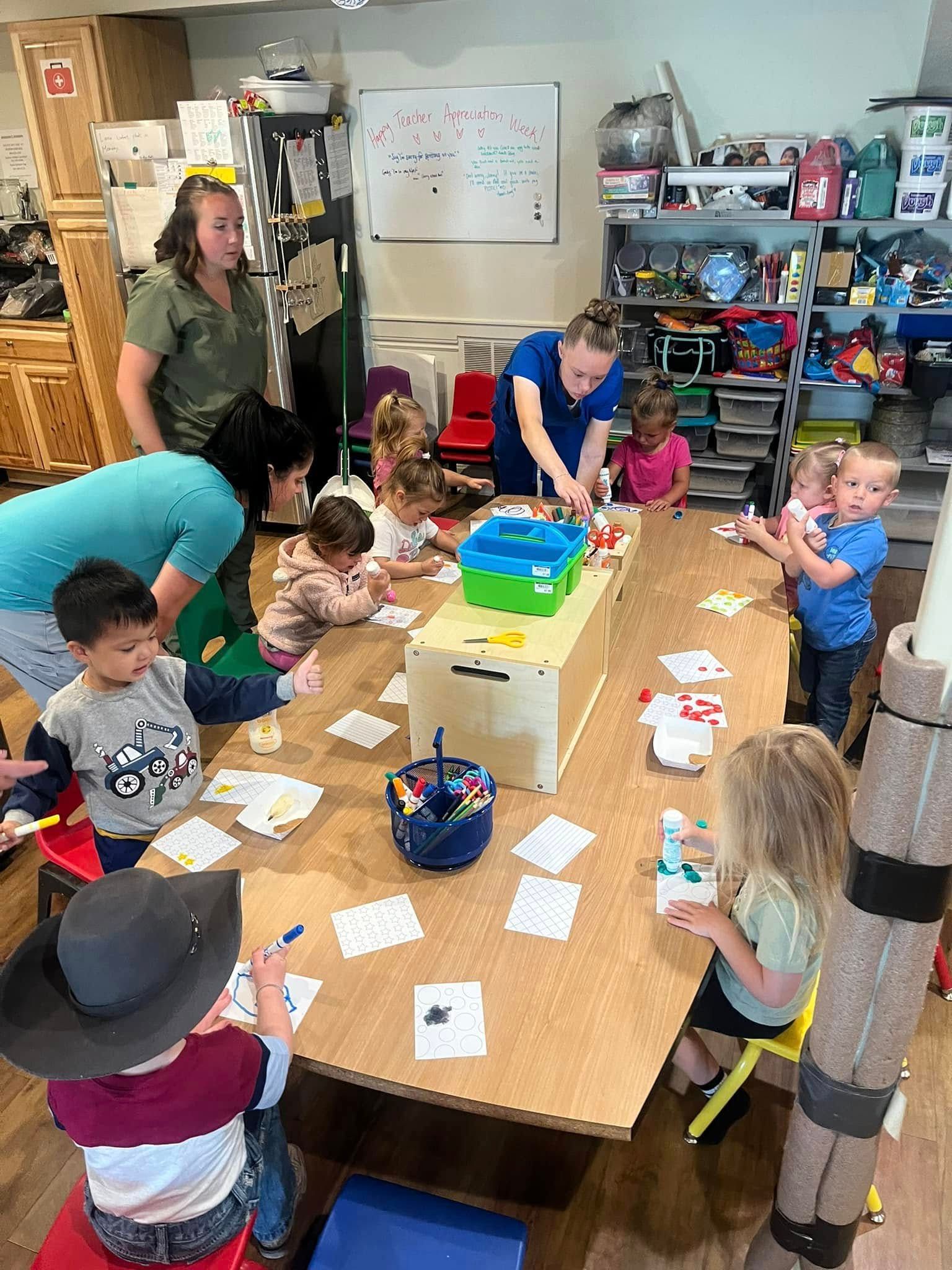 A group of children are sitting around a table in a classroom.