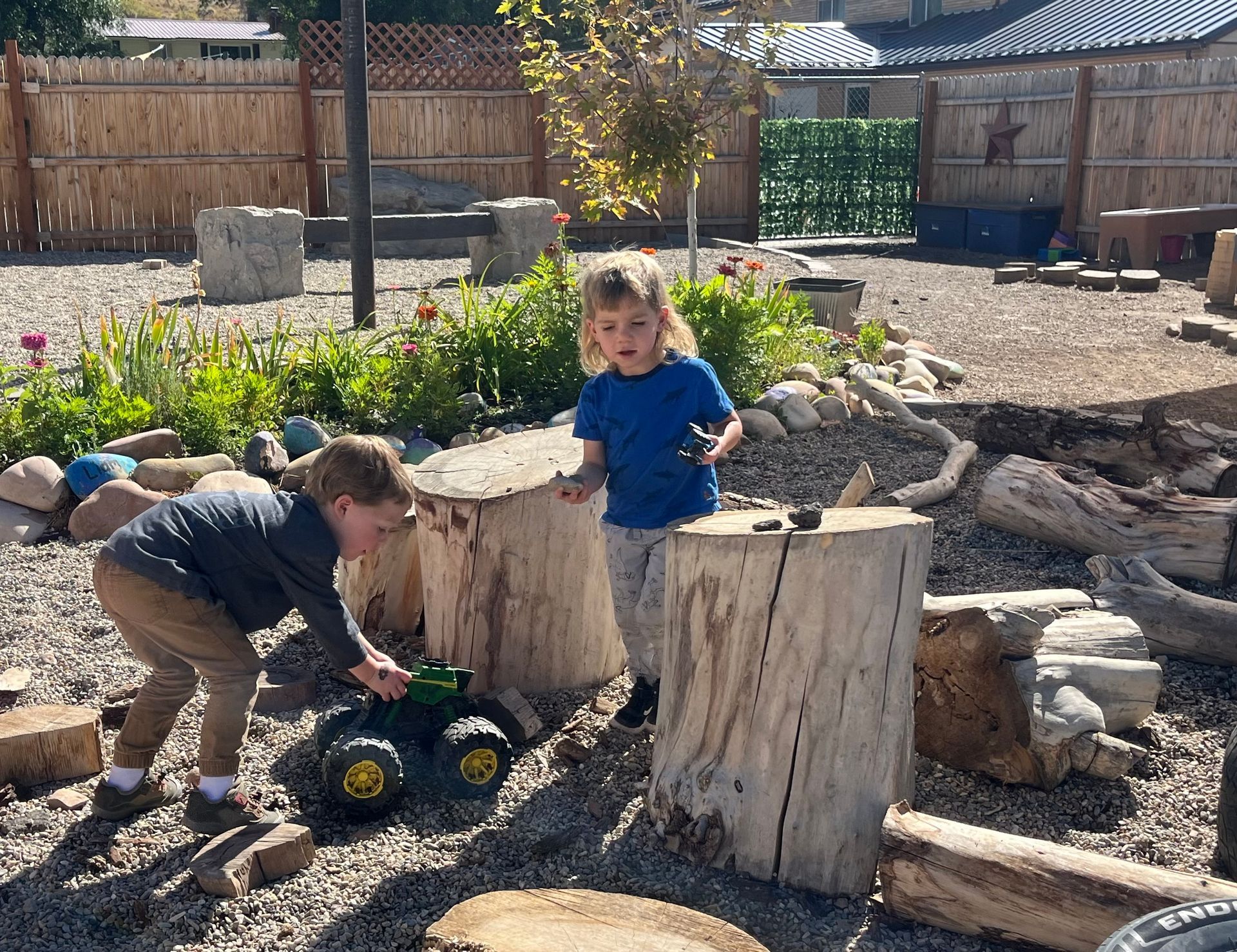 A group of children are sitting on the floor reading a book. Two children playing with toy truck and objects in outdoor play area.