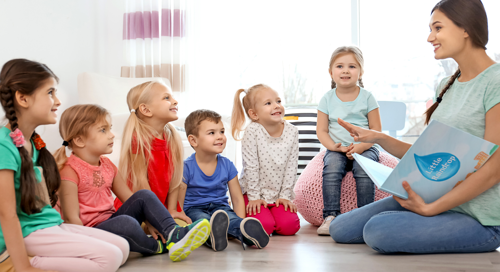 A woman is sitting on the floor reading a book to a group of children.