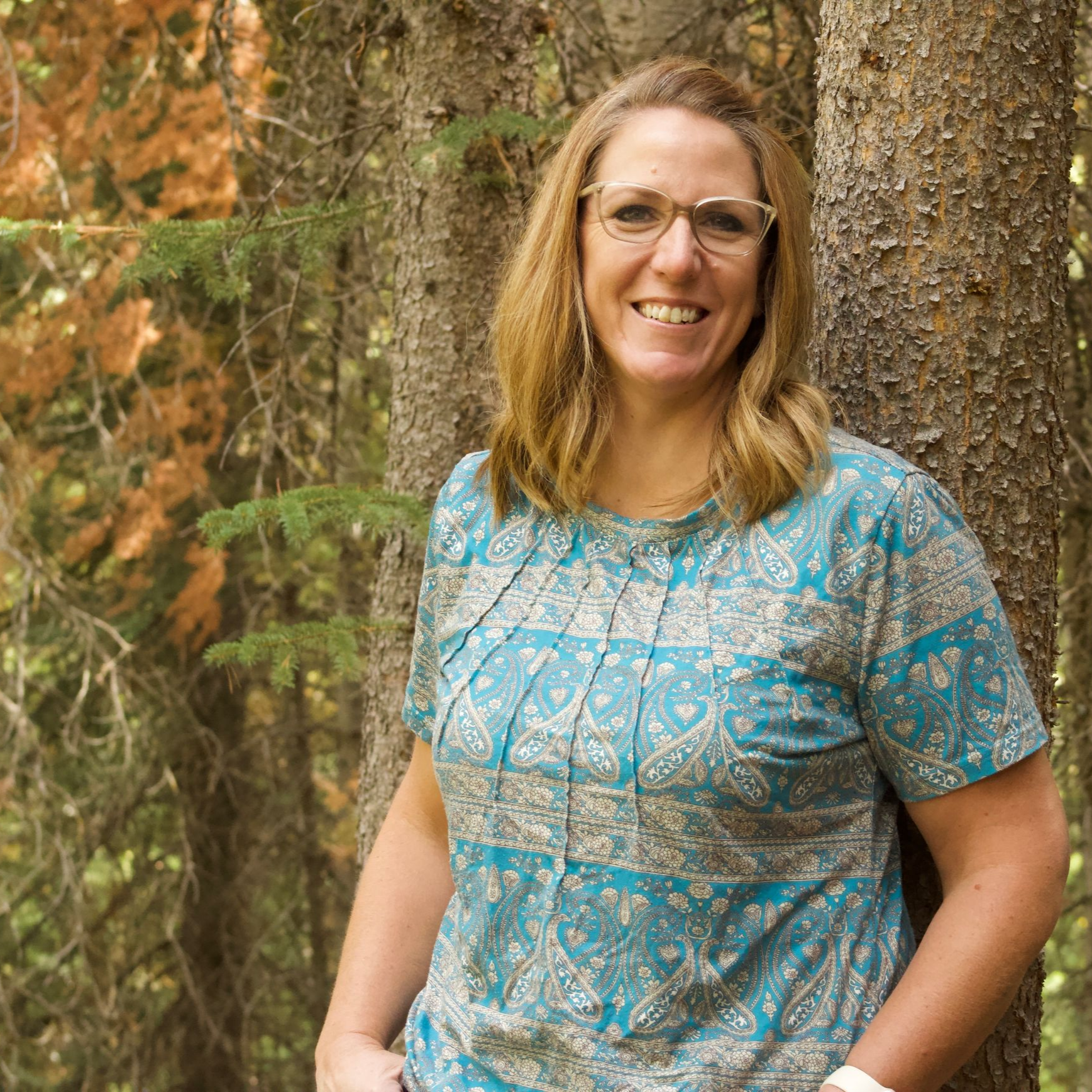 A woman wearing glasses and a necklace is smiling for the camera.