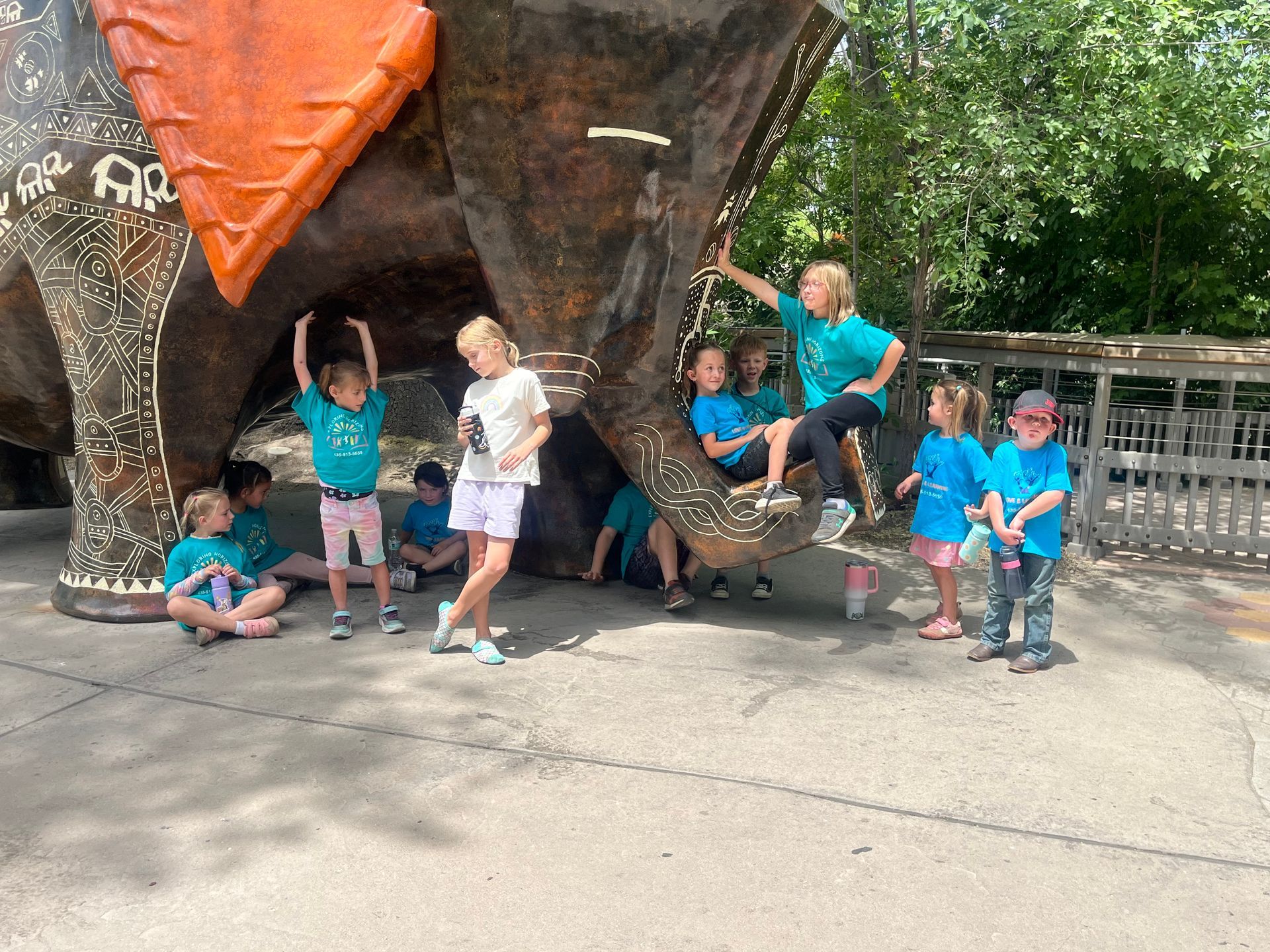 A group of children are standing in front of a dinosaur statue.