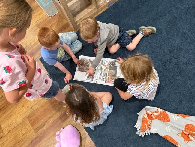 A group of children are sitting on the floor reading a book. A group of children are sitting on the floor reading a book.