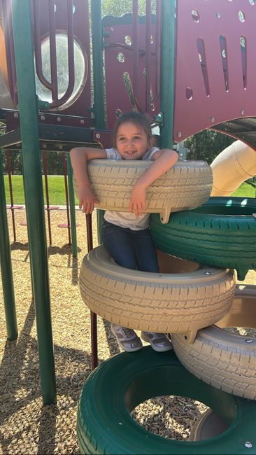 Child smiling while playing on a playground tire structure.