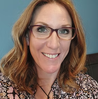 A woman wearing glasses and a necklace is smiling for the camera.