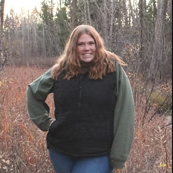 A woman in a black vest and green sweatshirt stands in a field