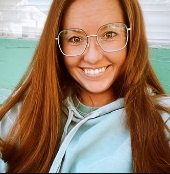 A woman wearing glasses and a blue hoodie is smiling for the camera.