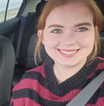 A woman in a striped sweater is smiling while sitting in the back seat of a car.