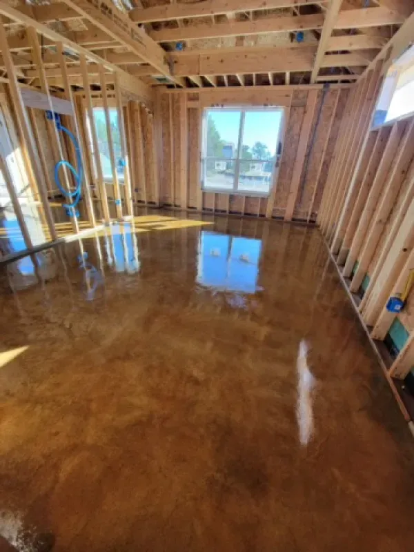 Room under construction with brown, glossy epoxy floor; wooden framing visible; sunlight through window.