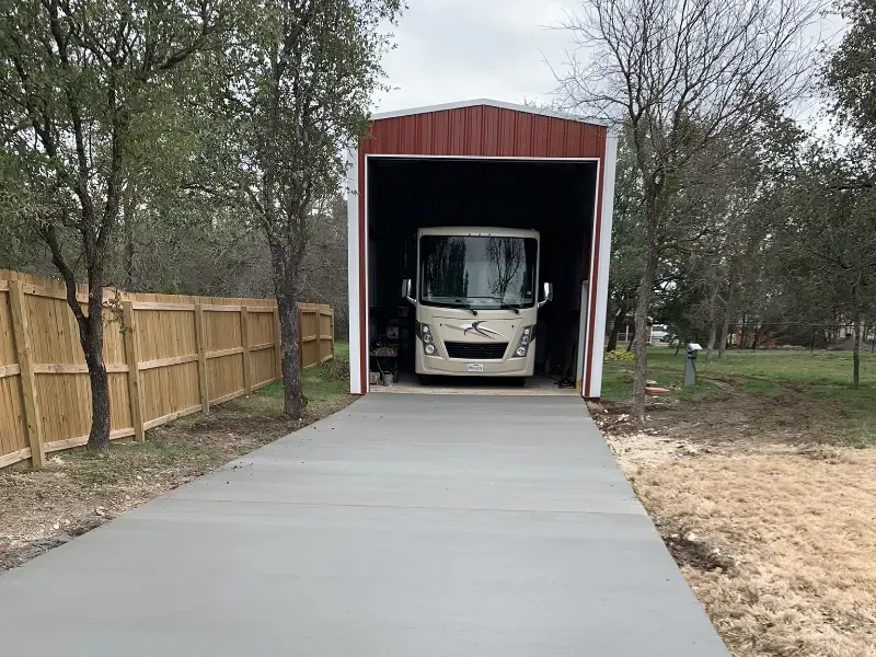 RV parked inside a red and white metal carport, with a concrete driveway.
