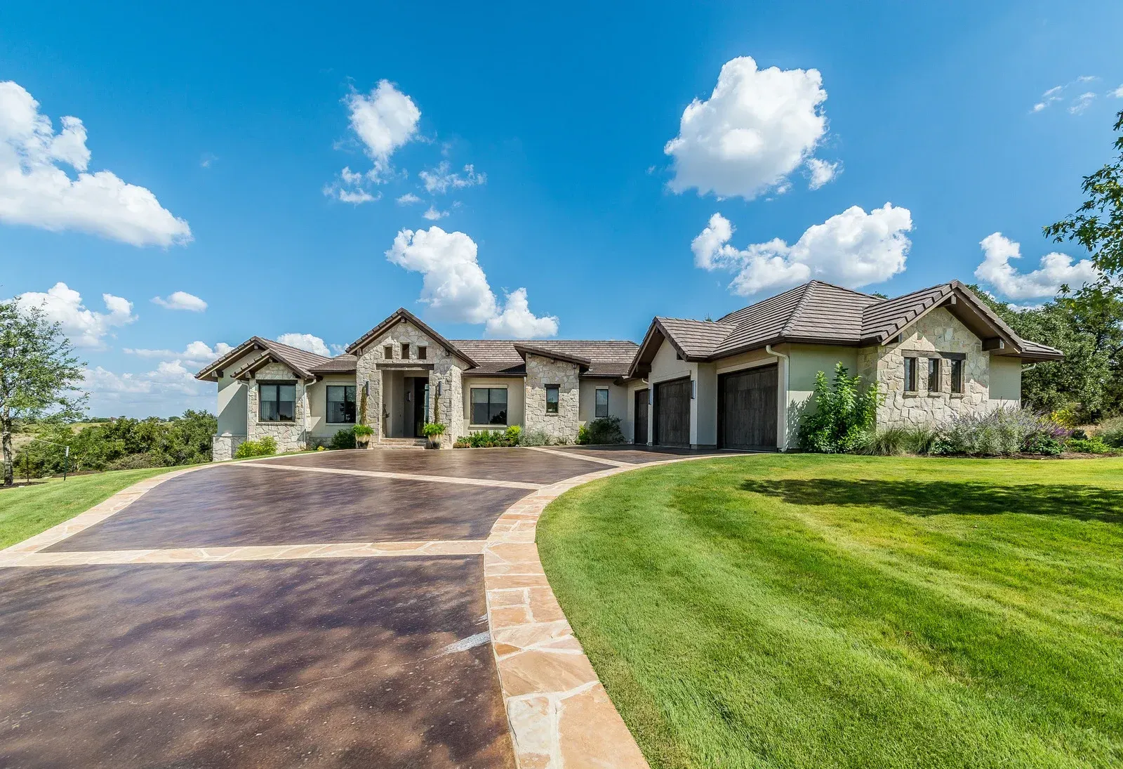 A large, stone home with a long, curved driveway on a bright, sunny day.