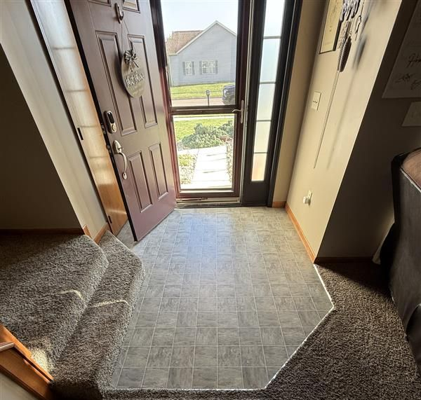 Front entryway with open door, carpeted steps, and a glass sidelight framing the view outside