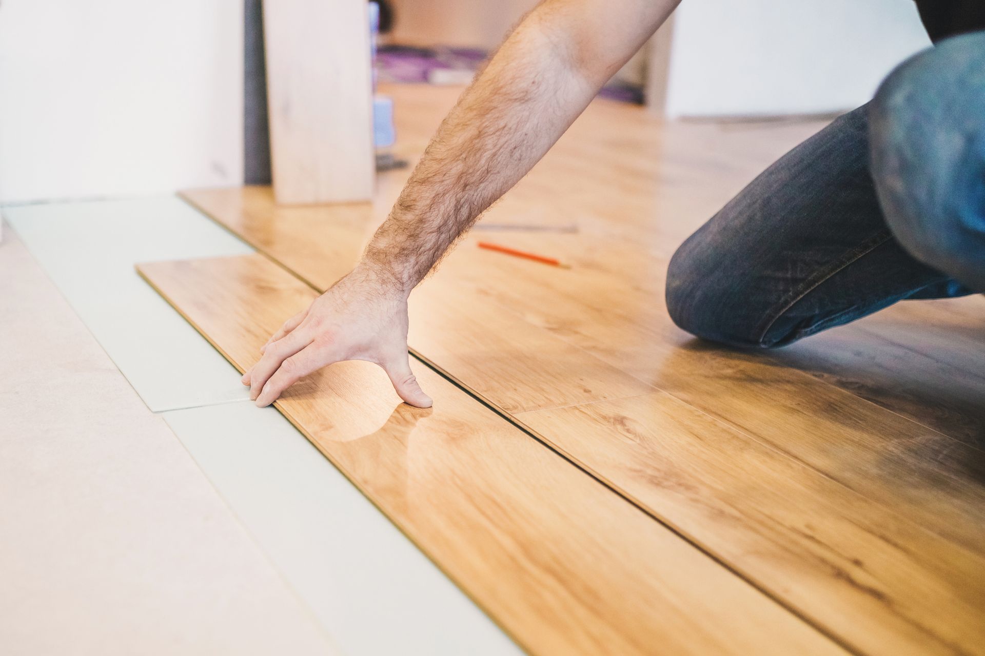 Person installing laminate flooring; they are kneeling, placing a wood plank over underlayment in a room.