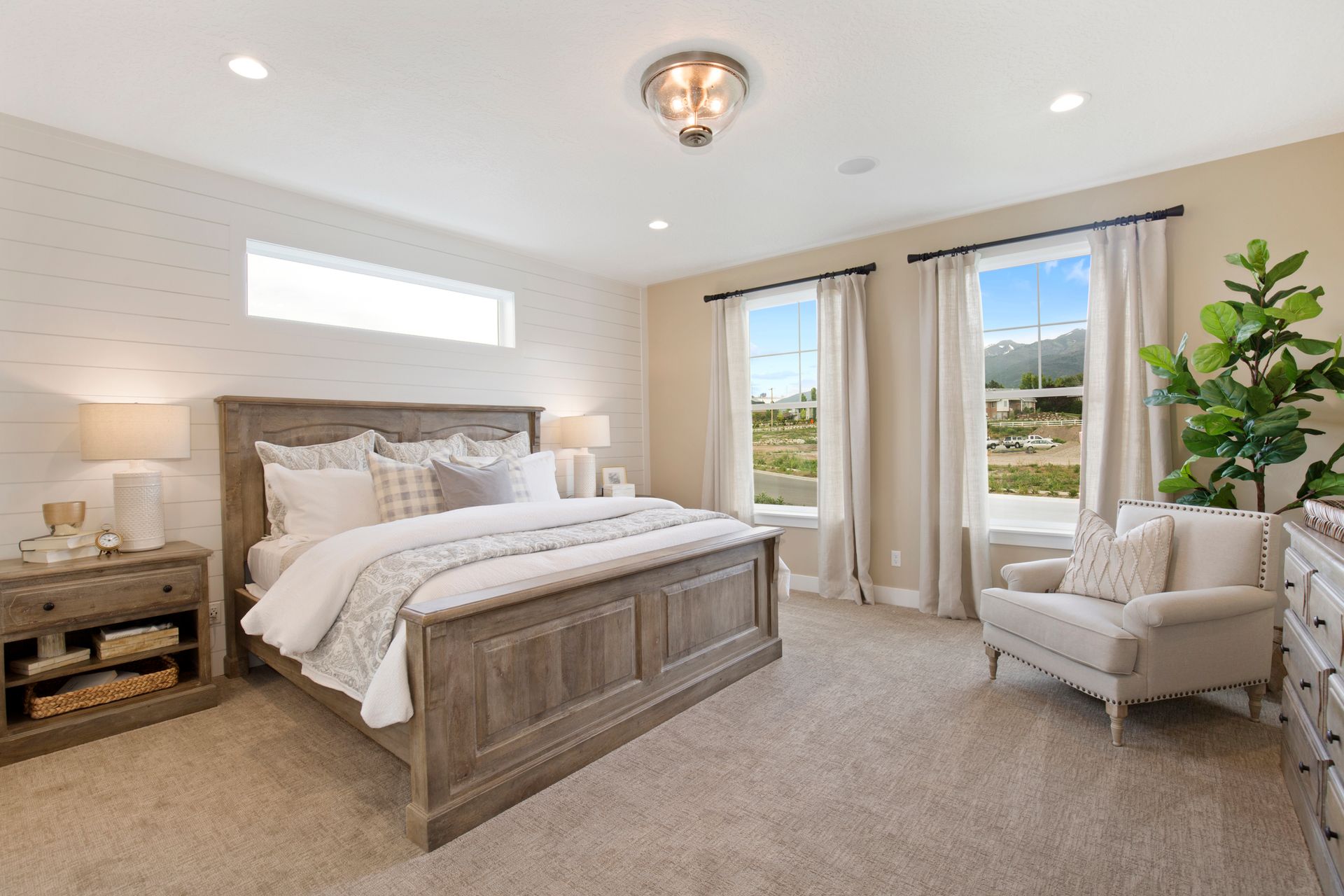 Bedroom with a gray wooden bed, beige walls, and a cozy armchair by the windows, with views of the outdoors.