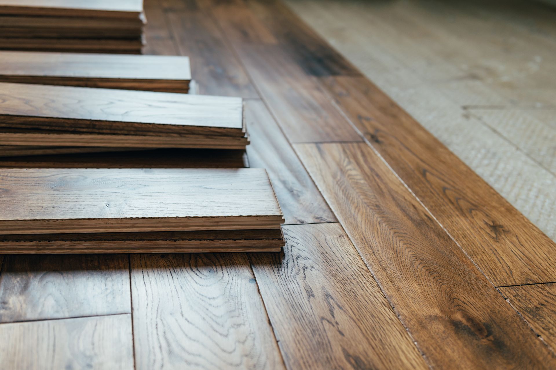 Wooden floor planks being installed, showing a stack of planks next to the finished flooring; warm brown tones.
