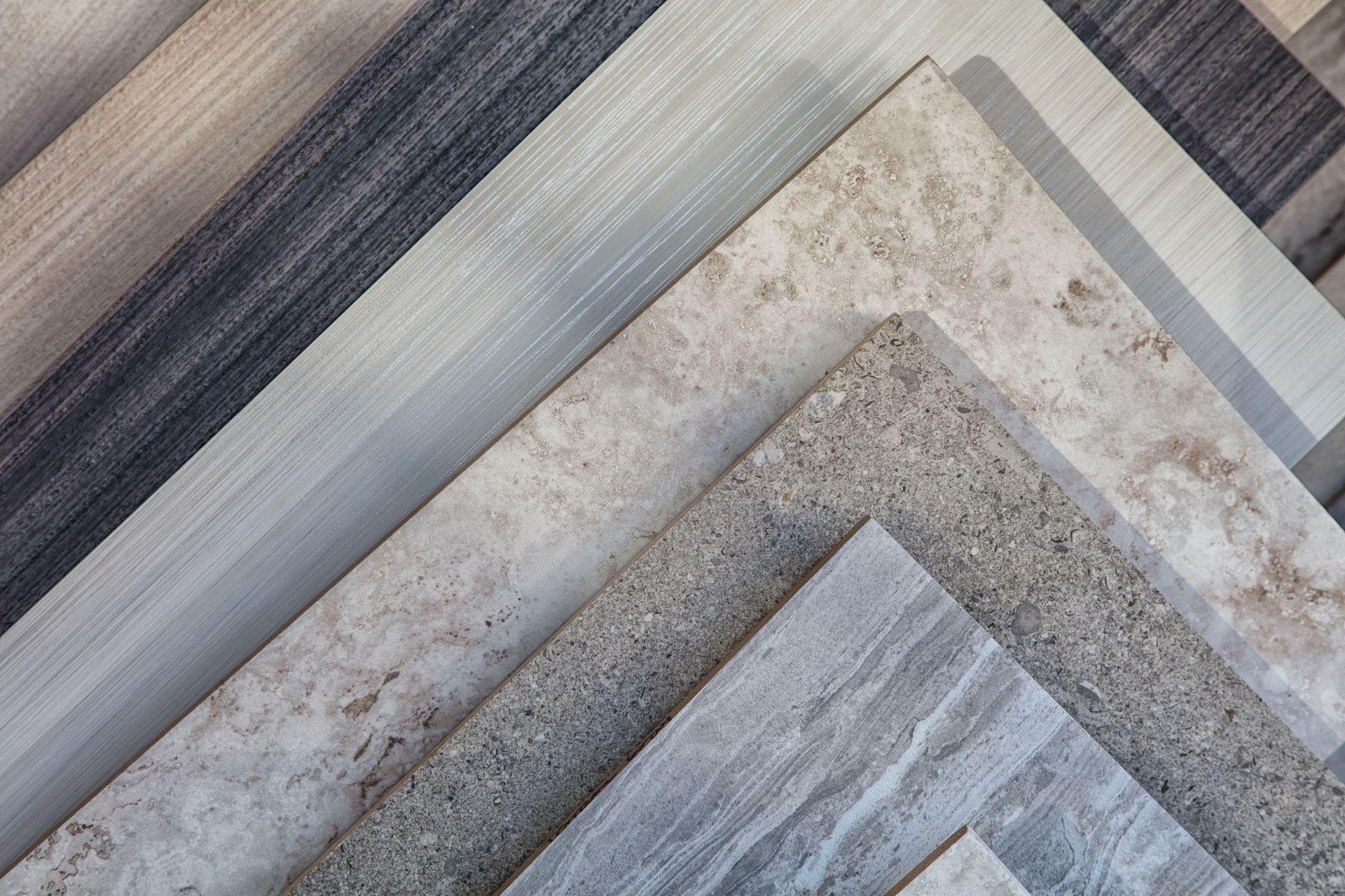 A collection of various tiles in neutral colors and textures, arranged in a layered diagonal display.
