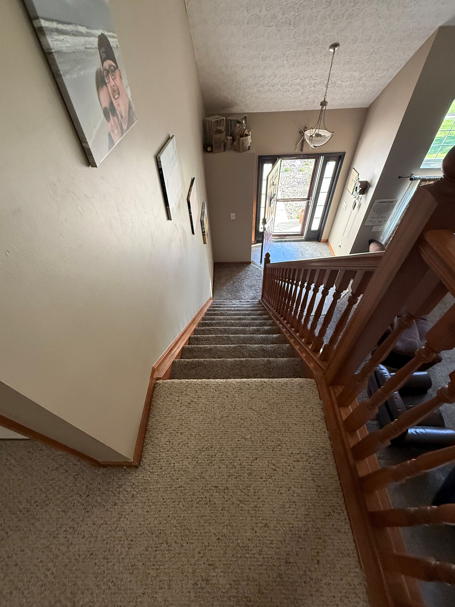 Interior entryway with carpeted stairs, wooden railing, and an open front door.