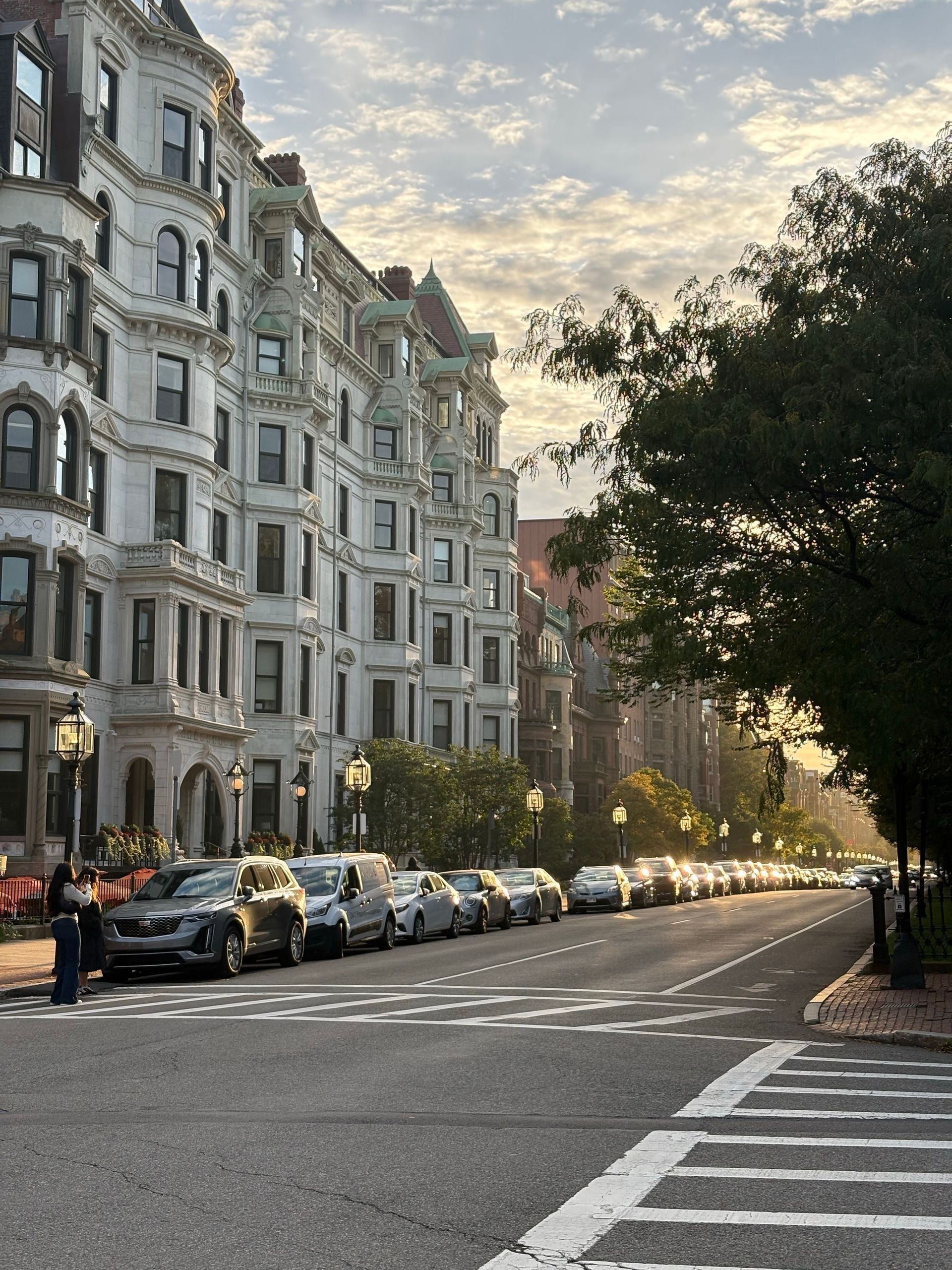 Sunlit city street lined with parked cars and white apartment buildings at dusk