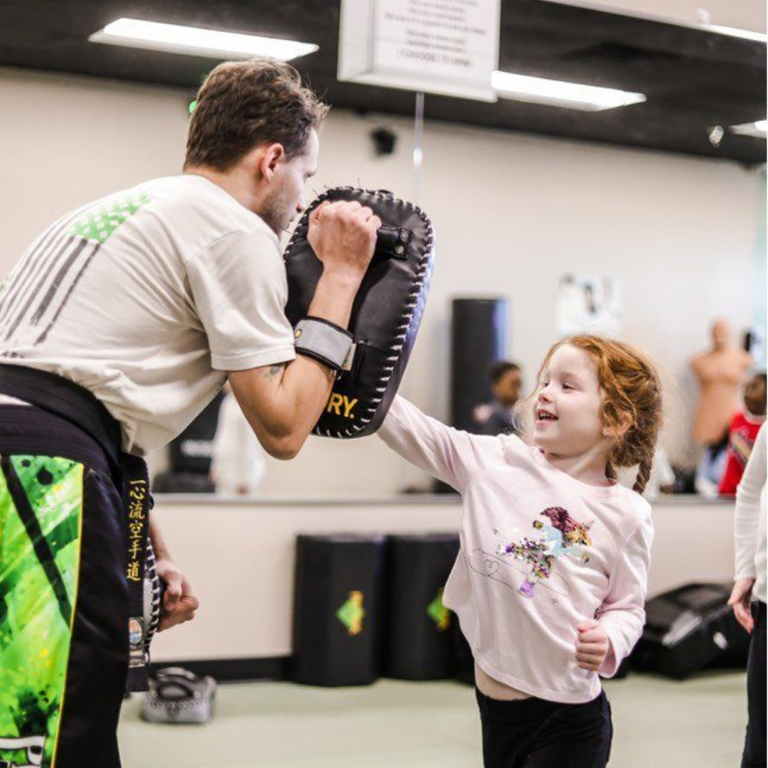 A young girl in a karate uniform is sitting on the floor.
