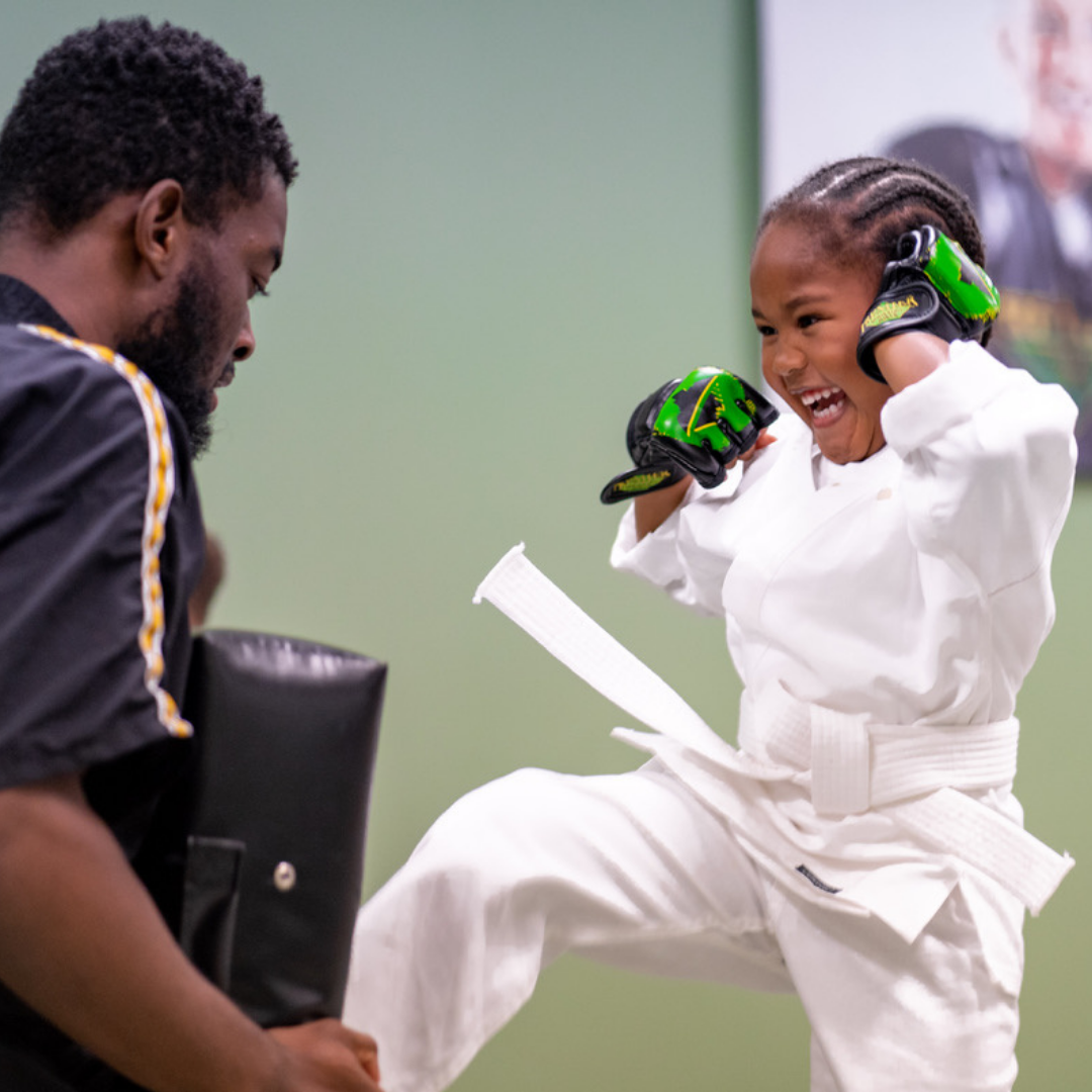 A group of children are practicing karate with a teacher in a gym.