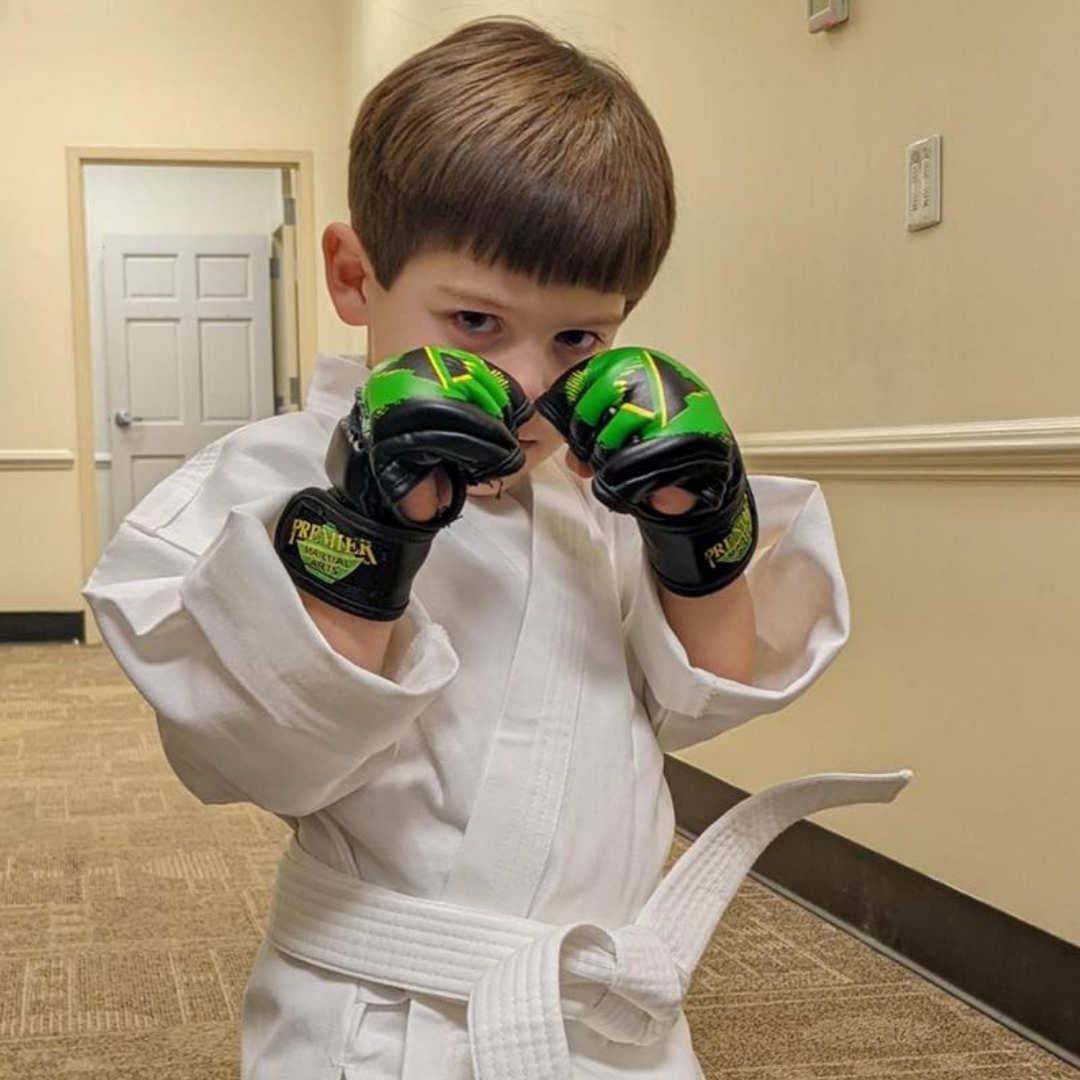 A man is kneeling down next to a young boy in a taekwondo class.