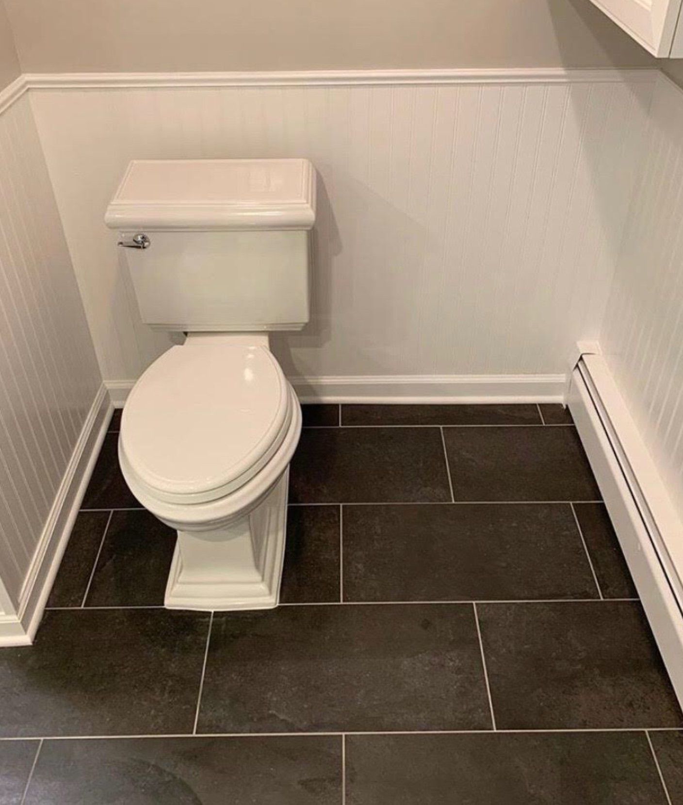 A white toilet is sitting on a black tiled floor in a bathroom.