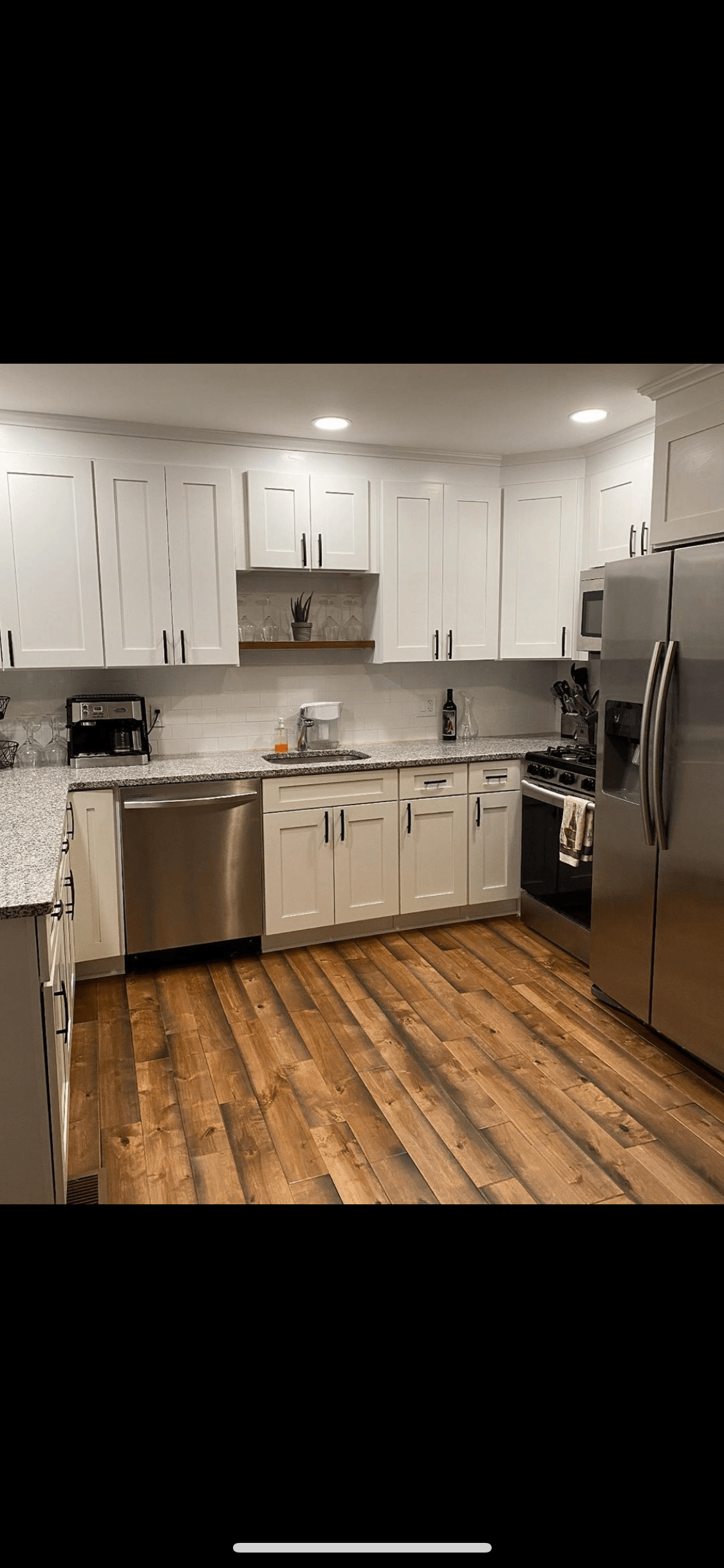 A kitchen with white cabinets , stainless steel appliances , and wooden floors.